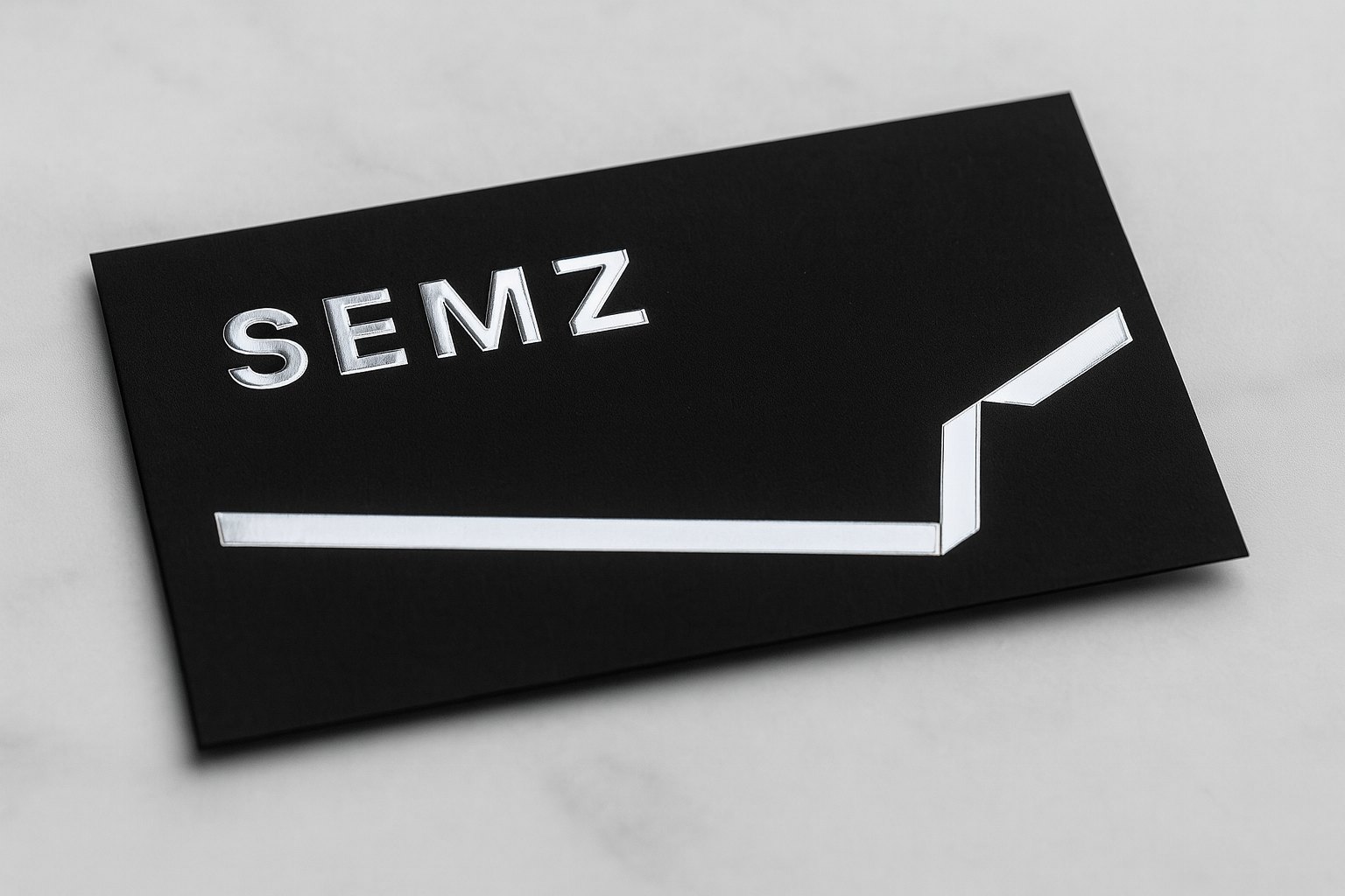 Black business card with silver foil logo, the foil catching the light against matte black